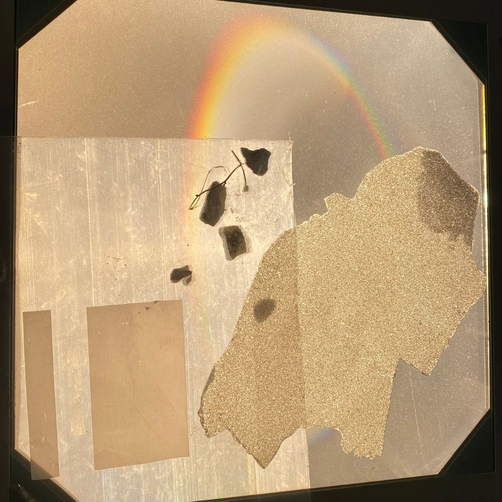 An abstract photomontage with torn paper shapes, shadows and a refracted rainbow